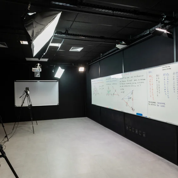 Estúdio preto, com lousa branca, com câmera filmadora e iluminação profissional