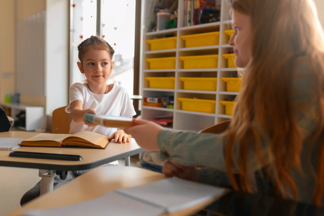 Adolescente entregando um livro para uma criança, simbolizando diferentes estágios do aprendizado escolar.