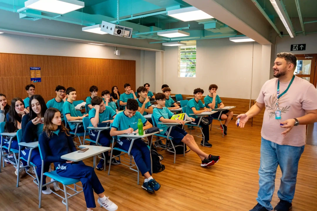 Alunos do Bernoulli sentados nas carteiras em sala de aula ouvindo o professor, que está de pé à frente
