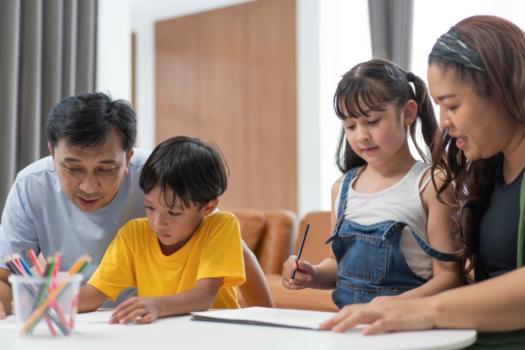 Família composta por pai, mãe e dois filhos estudando juntos em casa, demonstrando a parceria entre a família e a escola