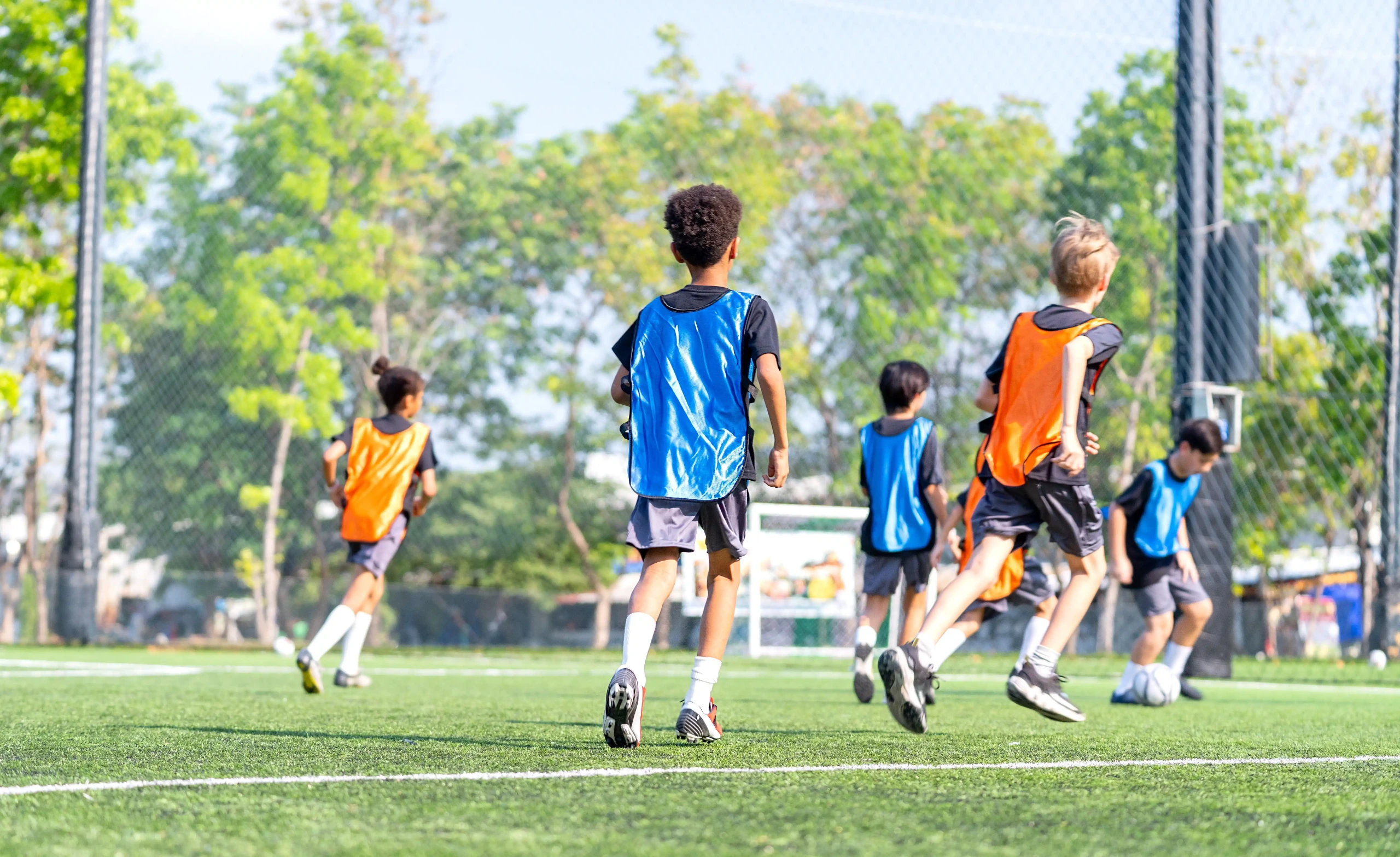 Grupo de alunos jogando futebol em um campo aberto, representando a importância da prática esportiva na escola
