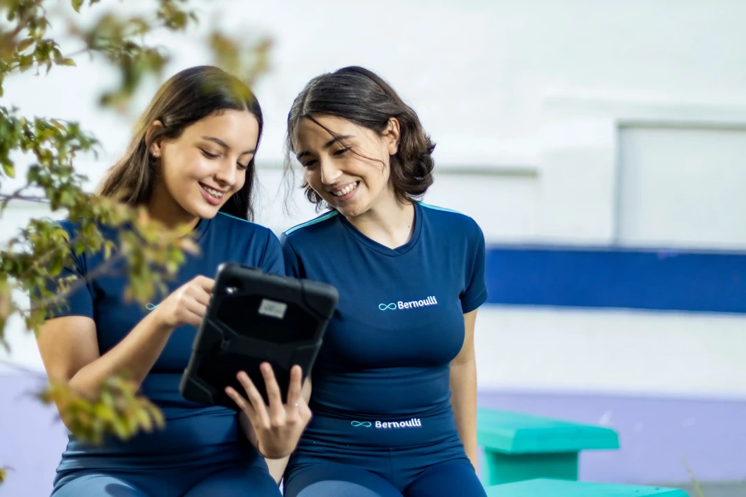 Alunas do Colégio Bernoulli lendo em um tablet, demonstrando como o hábito do estudo ajuda a melhorar o desempenho escolar