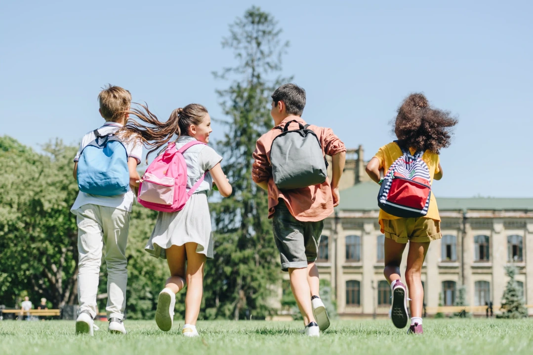 Estudantes brincando em um gramado com as mochilas nas costas, representando as férias escolares com equilíbrio entre descanso e aprendizado